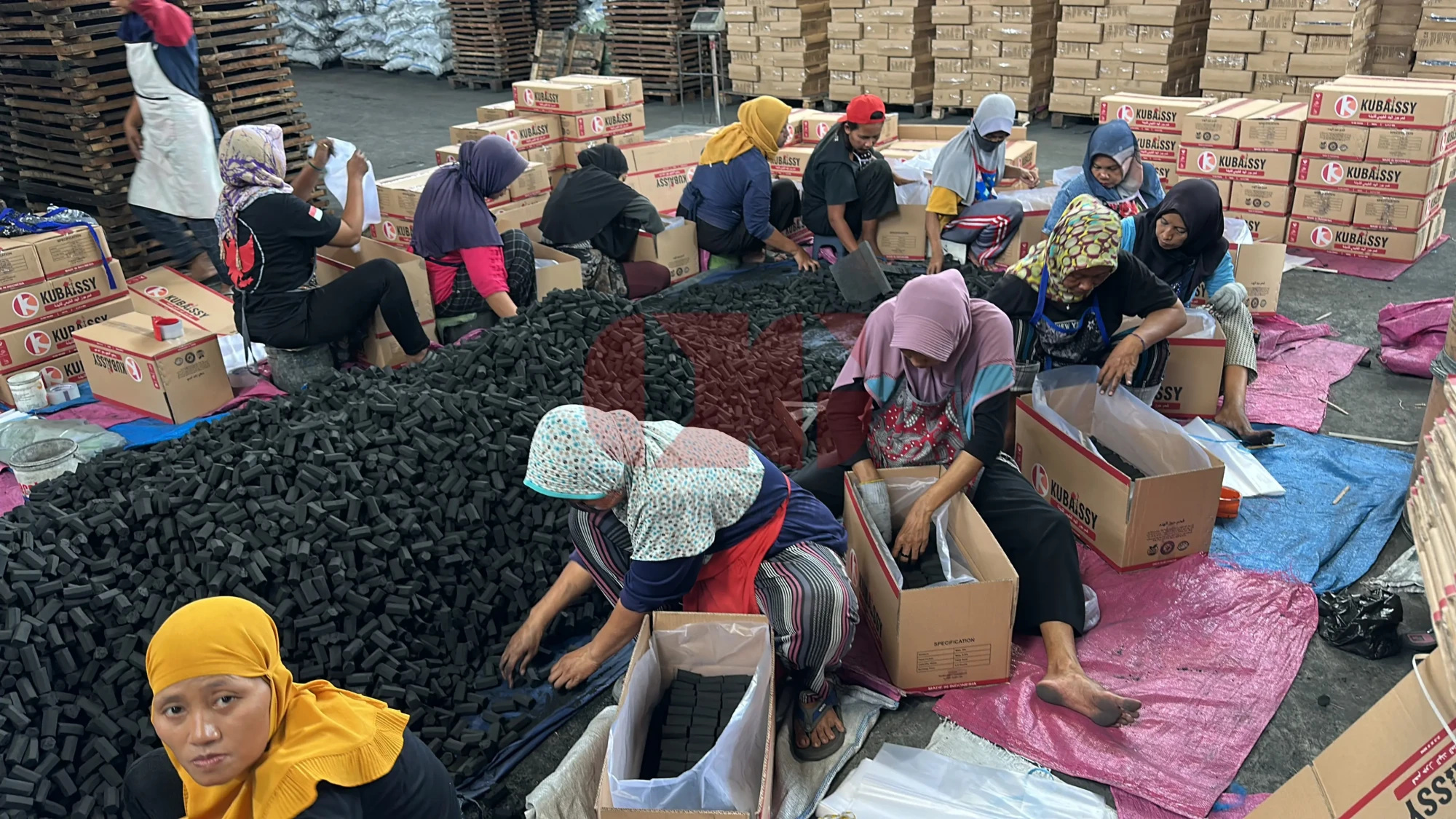 Workers performing quality control and sorting coconut shell charcoal briquettes.